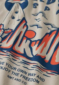 Bawełniana tkanina z kremowym tłem przedstawia graficzny nadruk gór, słońca i ptaków w odcieniach niebieskiego i pomarańczowego. Poniżej znajduje się tekst z detalami.