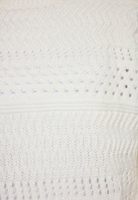Țesătură albă tricotată, având un model în zigzag combinat cu găuri decorative. Textură netedă cu un aspect ușor.