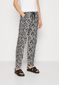 Svartvitt mönstrade byxor med elastisk midja och dragsnöre, med sidofickor och avslappnad passform. Bärs med svarta sandaler.