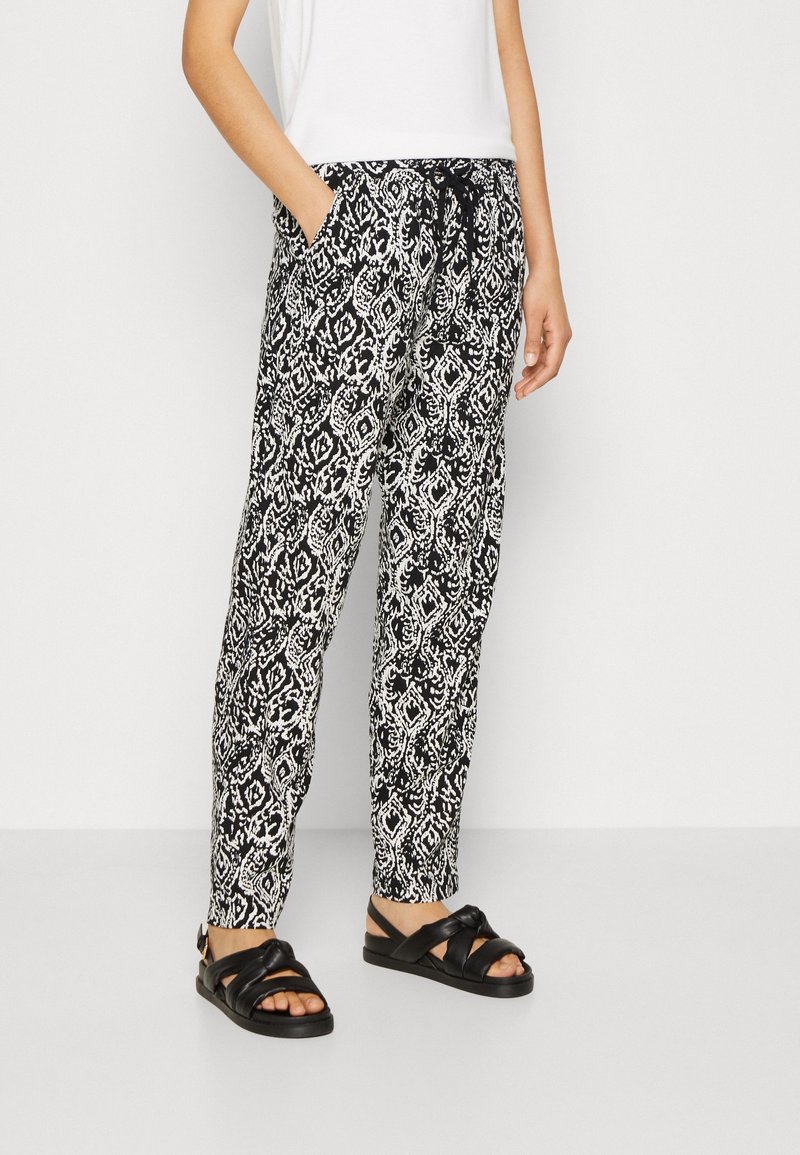 Svartvitt mönstrade byxor med elastisk midja och dragsnöre, med sidofickor och avslappnad passform. Bärs med svarta sandaler.