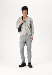 Helles graues Cardigan mit Knöpfen, kombiniert mit karierten grauen Hosen. Schwarze Tasche und Schuhe. Glatte Textur und lässige Passform.