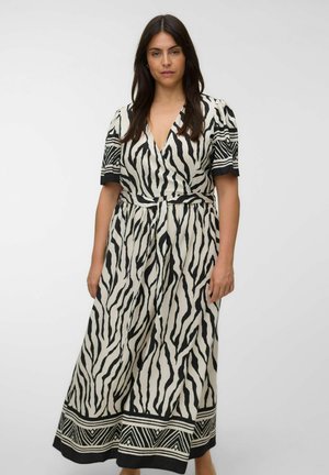 Jeune femme aux longs cheveux foncés portant une robe portefeuille imprimé zèbre noire et blanche avec manches courtes et bordure géométrique.