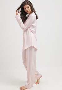 Conjunto de pijama rosa claro que incluye una camisa de botones de manga larga y pantalones de pierna ancha. Tejido suave y liso con un corte relajado y una textura brillante.