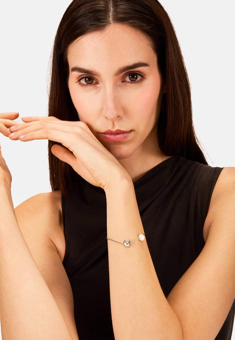 Pulsera de plata y perlas con dos cuentas redondas sobre una fina cadena, llevada en la muñeca contra una blusa negra, destacando un diseño minimalista.