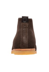 Braune Wildleder-Ankle Boots mit brauner Gummisohle, ausgestattet mit einer schwarzen Stoffschlaufe an der Ferse und geprägtem Branding an der Seite.