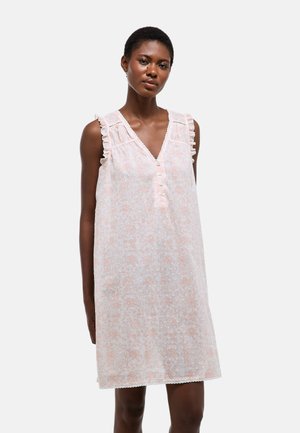 Femme portant une robe sans manches, rose pâle, longueur genou, avec broderies florales et détails de boutons sur fond blanc.