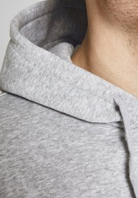 Grijze hoodie weergegeven met een close-up van de stoftextuur, de naad van de capuchon en de halslijn. Materiaal lijkt zacht en licht gemêleerd.