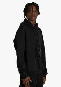 Felpa nera con cappuccio, dotata di tasca frontale con patta, chiusura con coulisse, tessuto morbido e polsini e orlo a coste.