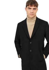 Schwarzer Wollmantel mit zwei Knöpfen, Reverskragen und seitlichen Taschen, getragen über einem gerippten beigen Rollkragenpullover. Glatte Textur und klassisches Design.