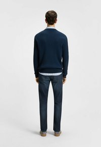 Navy ribbed sweater with a collar, layered over a light striped shirt. Paired with dark blue denim pants and gray shoes.