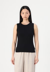 Black sleeveless top made of smooth fabric; features a round neck and a fitted silhouette, paired with light beige wide-leg trousers.