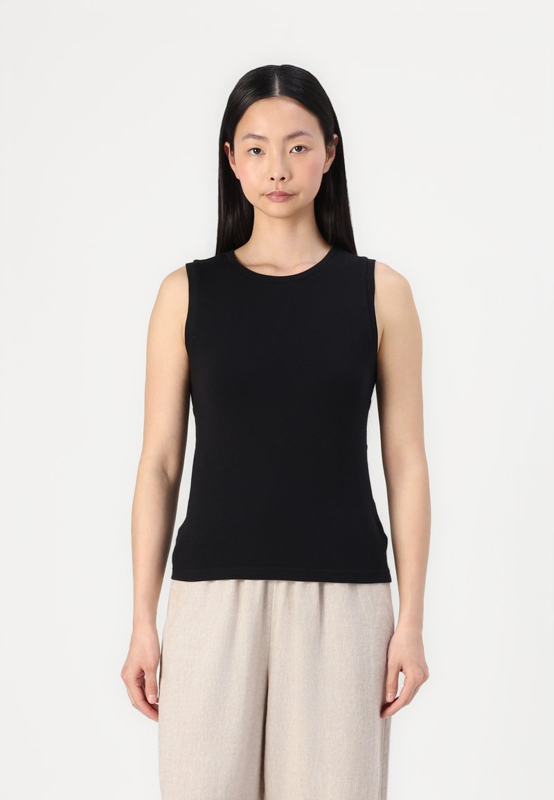 Black sleeveless top made of smooth fabric; features a round neck and a fitted silhouette, paired with light beige wide-leg trousers.