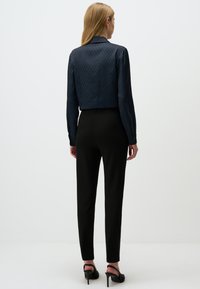 Marineblouse met een ruitpatroon, lange mouwen en een kraag, gecombineerd met zwarte getailleerde broeken en zwarte hoge hakken.
