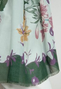 Kwiatowy szal z jasnozielonego materiału, zdobiony fioletowymi i pomarańczowymi kwiatami o misternych detalach, z frędzlami na dolnym brzegu.