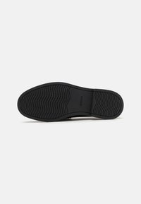 Suola di scarpa in gomma nera con superficie testurizzata e motivi ondulati, con logo di marca sul lato. Design piatto per stabilità.