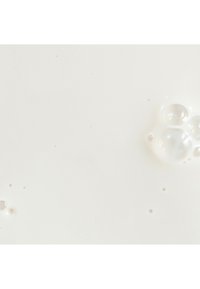 Liquide blanc avec de petites bulles et une texture de surface lisse, ressemblant à du lait ou de la crème, sur un fond clair et neutre.