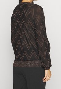 Maglione nero con un motivo a zigzag testurizzato in fili metallici, dotato di orlo a coste e maniche lunghe. Leggero e semi-trasparente.