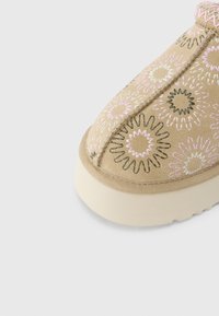 Μηχανοκίνητο μπουντουάρ σε μπεζ χρώμα με κεντημένα λουλουδάτα σχέδια σε ροζ, άσπρο και μαύρο πάνω σε μαλακό επάνω μέρος από ύφασμα και παχύ εξωτερικό υπόλευκο πάτο.