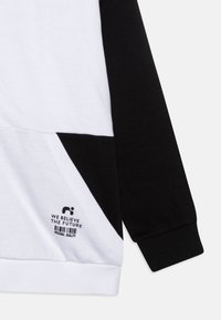 Felpa a maniche lunghe in bianco e nero realizzata in cotone. Presenta un pannello diagonale nero, un logo e dettagli testuali vicino all'orlo.