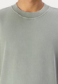 Sweatshirt verde claro com gola redonda, apresentando uma textura suave e colarinho canelado. Design minimalista, sem padrões ou acessórios visíveis.