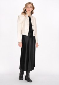 Kremfarvet læderjakke i cropped stil med tre knapper, båret over en sort satin kjole, parret med sorte ankelstøvler. Enkel, tætsiddende design.