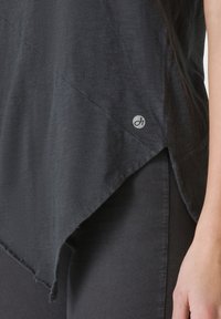 Top texturat negru cu o margine asimetrică, având un logo subtil pe lateral și detalii vizibile de cusătură.