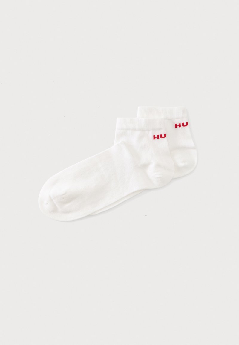 Deux paires de chaussettes blanches à la cheville avec le texte rouge "HU" près du bord-côte sur un fond uni clair.