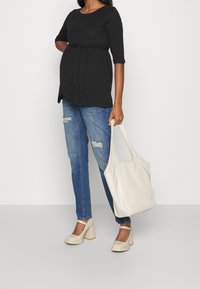 Svart graviditetströja med knytmidja, blå slitna jeans, beiga klackskor med blockhäl och en vit tote bag.