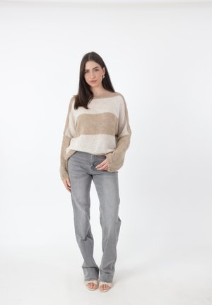 Beige en crèmekleurige gestreepte gebreide trui met brede mouwen, gecombineerd met lichtgrijze denim jeans. De stof lijkt zacht en heeft een comfortabele pasvorm.