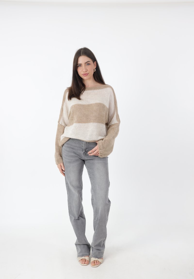 Maglione a righe beige e crema con maniche ampie, abbinato a jeans in denim grigio chiaro. Il tessuto sembra morbido con una vestibilità rilassata.