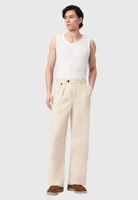 Weißes, geripptes Tanktop, kombiniert mit beigen, weit geschnittenen Hosen mit Falten und doppelter Knopfverschluss, dazu braune, strukturierte Schuhe.