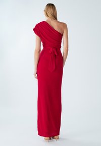 Dlhé priliehavé červené šaty s asymetrickým jednorameným dizajnom, zdobené záhybmi látky a viazaným detailom v páse. Hladká textúra, dĺžka po zem.