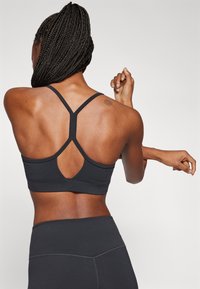 Sutiã desportivo preto com um design de costas nadador e um recorte em forma de chave. Textura suave e forma ajustada, combinado com leggings pretas de cintura alta.