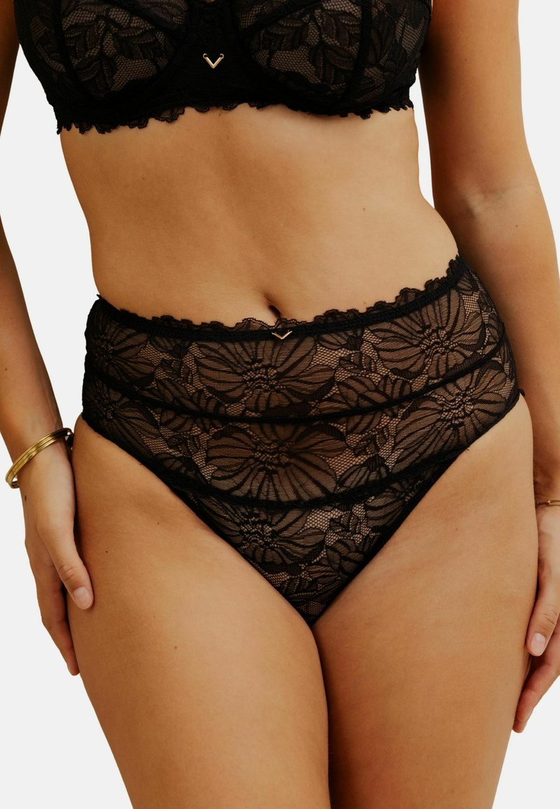 Bralette en dentelle noire et culottes taille haute avec motif floral, bords festonnés et un détail en or entre les couches de tissu.