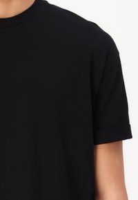 Černé bavlněné tričko s kulatým výstřihem, krátkými ohrnutými rukávy a hladkou strukturou. Minimalistický design bez viditelných log.