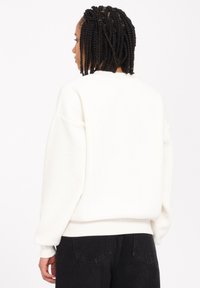 Hvid sweatshirt lavet af blødt materiale, med en afslappet pasform, ribbede manchetter og kant. Bæres med sorte højtaljede jeans.