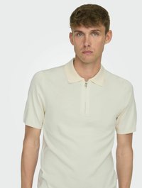 Polo shirt in crema testurizzata con colletto corto e mezza cerniera. Design aderente con maniche corte, che mette in risalto uno stile minimalista.
