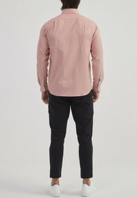 Chemise à rayures rouges et blanches à manches longues avec des poignets à boutons, coupe ajustée et col classique, associée à un pantalon noir et des baskets blanches.