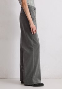 Szare szerokie spodnie o gładkiej fakturze, z tapered talią i kieszeniami po bokach, w połączeniu z czarnymi butami na szpilce.