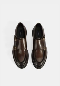 Braune Lederschuhe mit glatter Oberfläche, runder Zehenpartie, doppelten Schnallen und kontrastierender schwarzer Sohle. Minimalistisches Design, keine sichtbaren Muster.