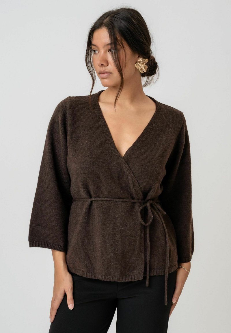 Brauner Wickeloberteil aus weichem Stoff, mit tiefem V-Ausschnitt, dreiviertel Ärmeln und einer Bindegürtel. Glatte Textur mit lässiger Passform.