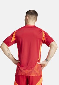 Maglia atletica rossa con accenti arancioni, maniche corte e un motivo testurizzato sulla parte bassa della schiena. Realizzata in materiale leggero e traspirante.