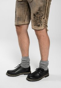 Pantaloni corti in pelle marrone con ricami floreali neri, abbinati a scarpe in pelle nera e calze lavorate a maglia grigie.