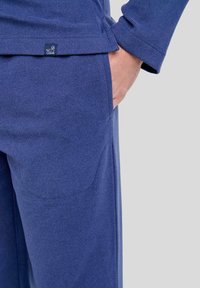 Pantalones informales azul marino con tejido texturizado, que cuentan con bolsillos laterales y una etiqueta con el logo. El diseño incluye un corte recto y líneas limpias.