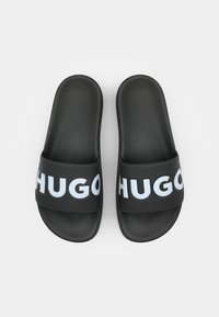 Sorte slidesandaler lavet af tekstureret gummi med en bred strop, der viser ordet "HUGO" i lyseblå. Flad sål uden synlige metaldele.
