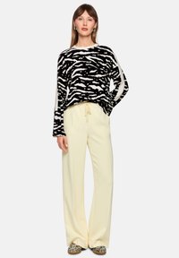 Black and white zebra-striped knit sweater paired with yellow wide-leg trousers, featuring drawstring waist and subtle sheen.