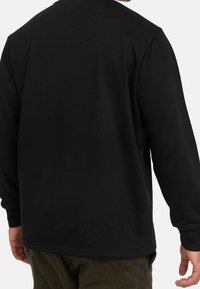 Maglietta nera a maniche lunghe realizzata in materiale morbido, con un design semplice, scollo rotondo e polsini a coste. Presenta una vestibilità comoda.