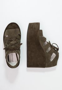 Sandales à plateforme en suede marron avec des côtés ouverts, un design à lacets et un talon compensé élevé. Dessus texturé et doublure intérieure lisse.