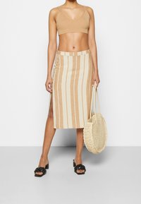 Beige ribbat crop top parat med en randig midi kjol i beige och krämfärg med sidofickor och knappar. Accessoarer med en vävd väska.