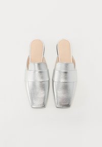 Sølvmetalliske slingback mules med teksturert finish, firkantet tå og bred stropp over vristen. Glatt beige innsåle synlig.